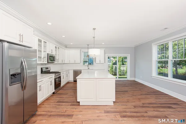 a kitchen with stainless steel appliances granite countertop a stove a sink dishwasher a refrigerator white cabinets and wooden floor