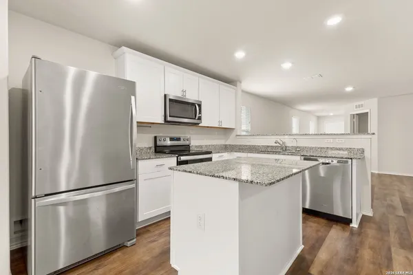 a kitchen with stainless steel appliances granite countertop a refrigerator a stove a sink a microwave and white cabinets with wooden floor