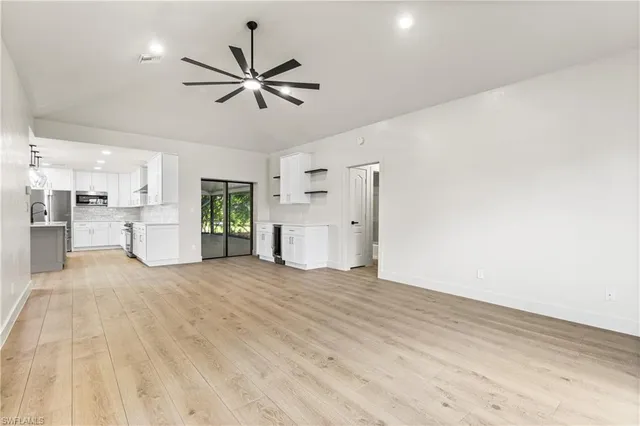 a view of a livingroom with a ceiling fan & kitchen space