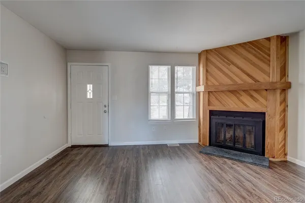 an empty room with wooden floor fireplace cabinet and windows