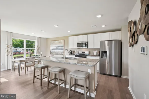 a kitchen with stainless steel appliances granite countertop a refrigerator a stove top oven a sink dishwasher and white cabinets with wooden floor