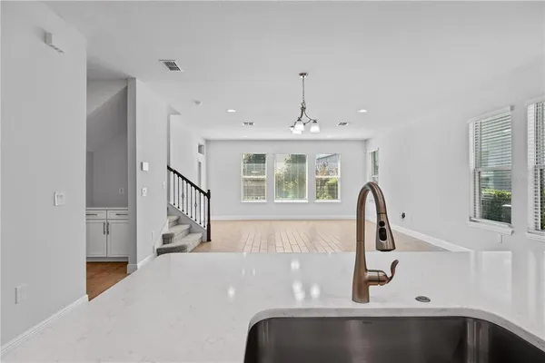 a view of an empty room and a kitchen with wooden floor