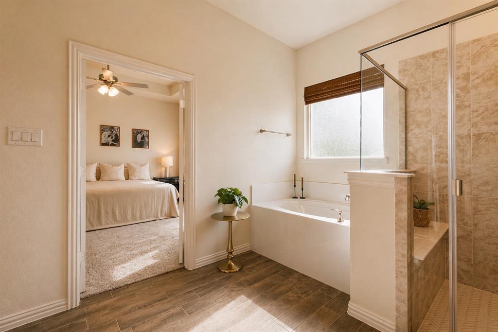 1530 County Road 200 Valley View, TX 76272 - Photo 25 of 34 Bright bathroom featuring a built-in soaking tub with a window, a glass-enclosed shower with tile surround, and wood-finish flooring