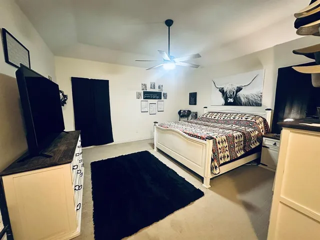 a spacious bedroom with a bed and a flat tv screen on the dresser