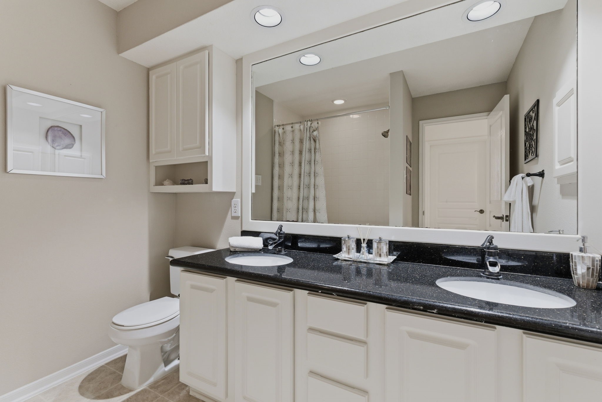 11 Dovewing Place Spring, TX 77382 - Photo 23 of 32 This bathroom features dual sinks with a sleek black countertop, ample cabinetry for storage, a large mirror, and modern lighting. The neutral color palette and elegant fixtures create a clean, sophisticated look.