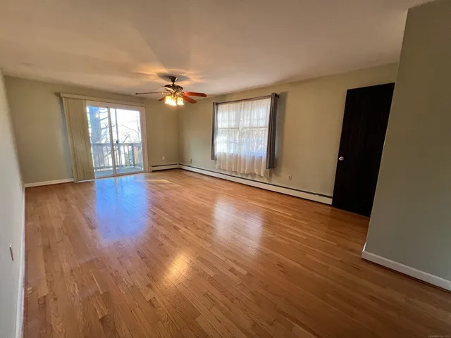 an empty room with wooden floor ceiling fan and windows