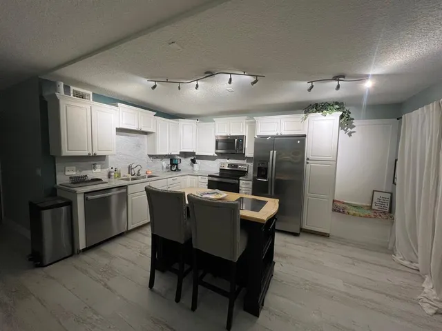 a kitchen with stainless steel appliances a refrigerator a stove a sink dishwasher and a dining table with wooden floor