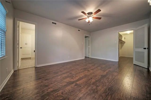 a view of an empty room with wooden floor and a ceiling fan