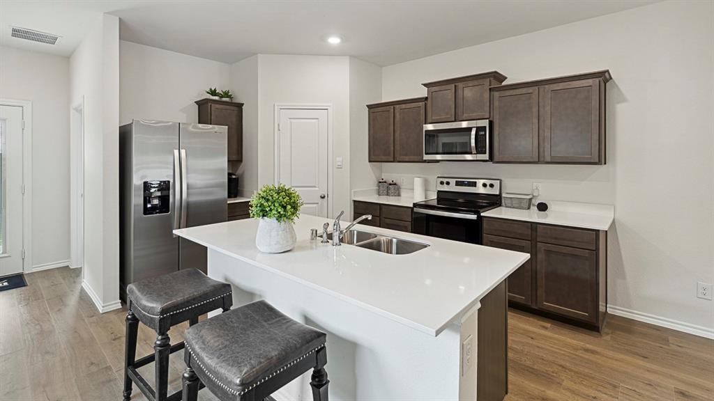 120 Pheasant Run Road Lavon, TX 75166 - Photo 6 of 17 Kitchen with stainless steel appliances, a kitchen breakfast bar, dark wood finish cabinetry, a kitchen island with sink, and light wood-type flooring
