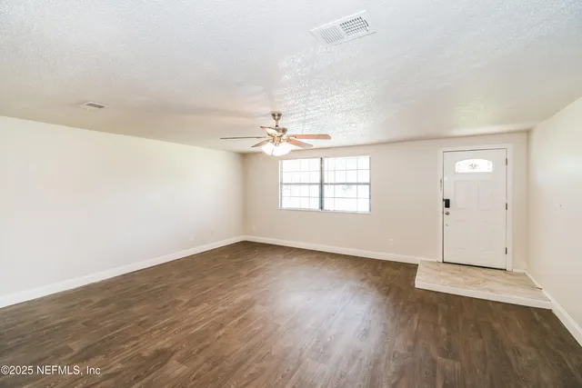 an empty room with wooden floor chandelier fan and windows