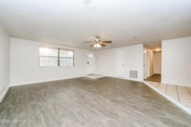 an empty room with wooden floor ceiling fan and windows