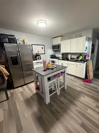 a room with stainless steel appliances kitchen island granite countertop a refrigerator a stove a sink dishwasher and white cabinets with wooden floor