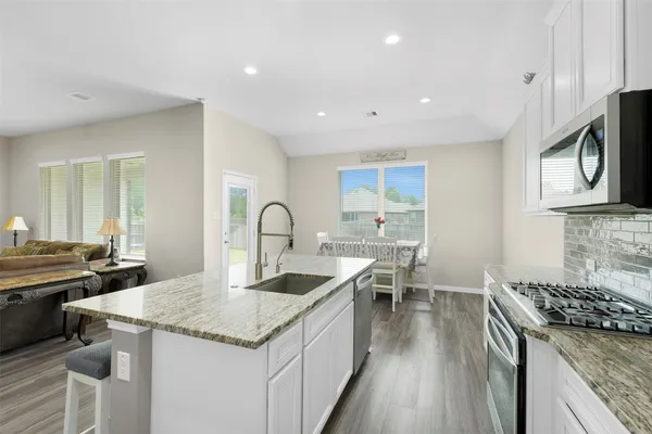 a kitchen with granite countertop a stove top oven a sink dishwasher and white cabinets with wooden floor