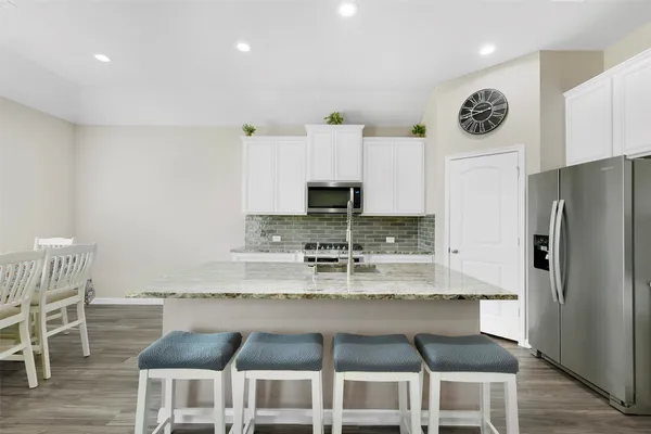 a kitchen with kitchen island granite countertop a dining table chairs and a refrigerator
