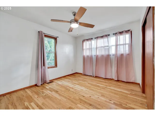 an empty room with wooden floor fan and windows
