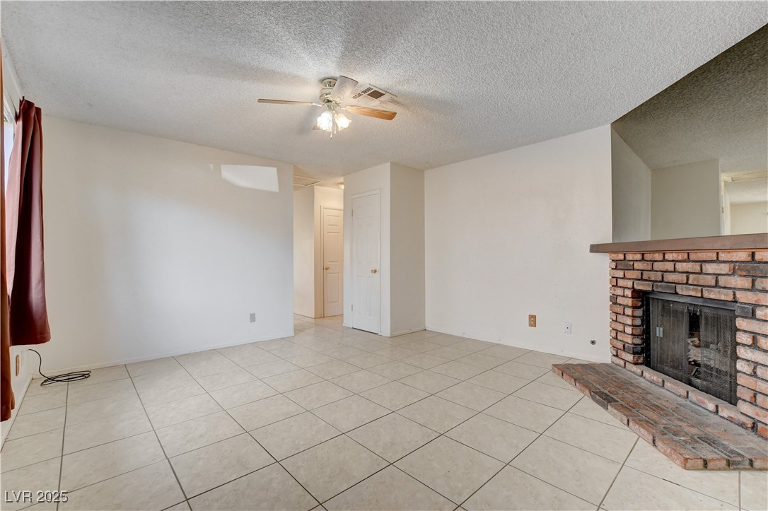 511 Chelsea Drive Henderson, NV 89014 - Photo 3 of 21 Unfurnished living room featuring a textured ceiling, light tile patterned flooring, a fireplace, and a ceiling fan