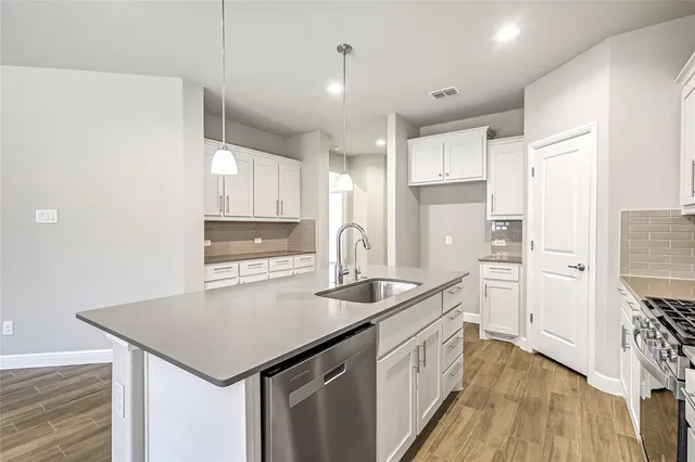 a kitchen with a sink dishwasher a refrigerator and white cabinets with wooden floor