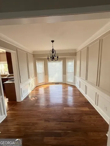 a view of empty room with wooden floor and kitchen