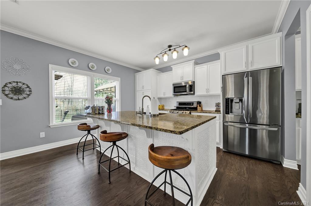a kitchen with granite countertop a refrigerator a stove a dining table and chairs with wooden floor