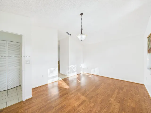 a view of an empty room with wooden floor and a ceiling fan