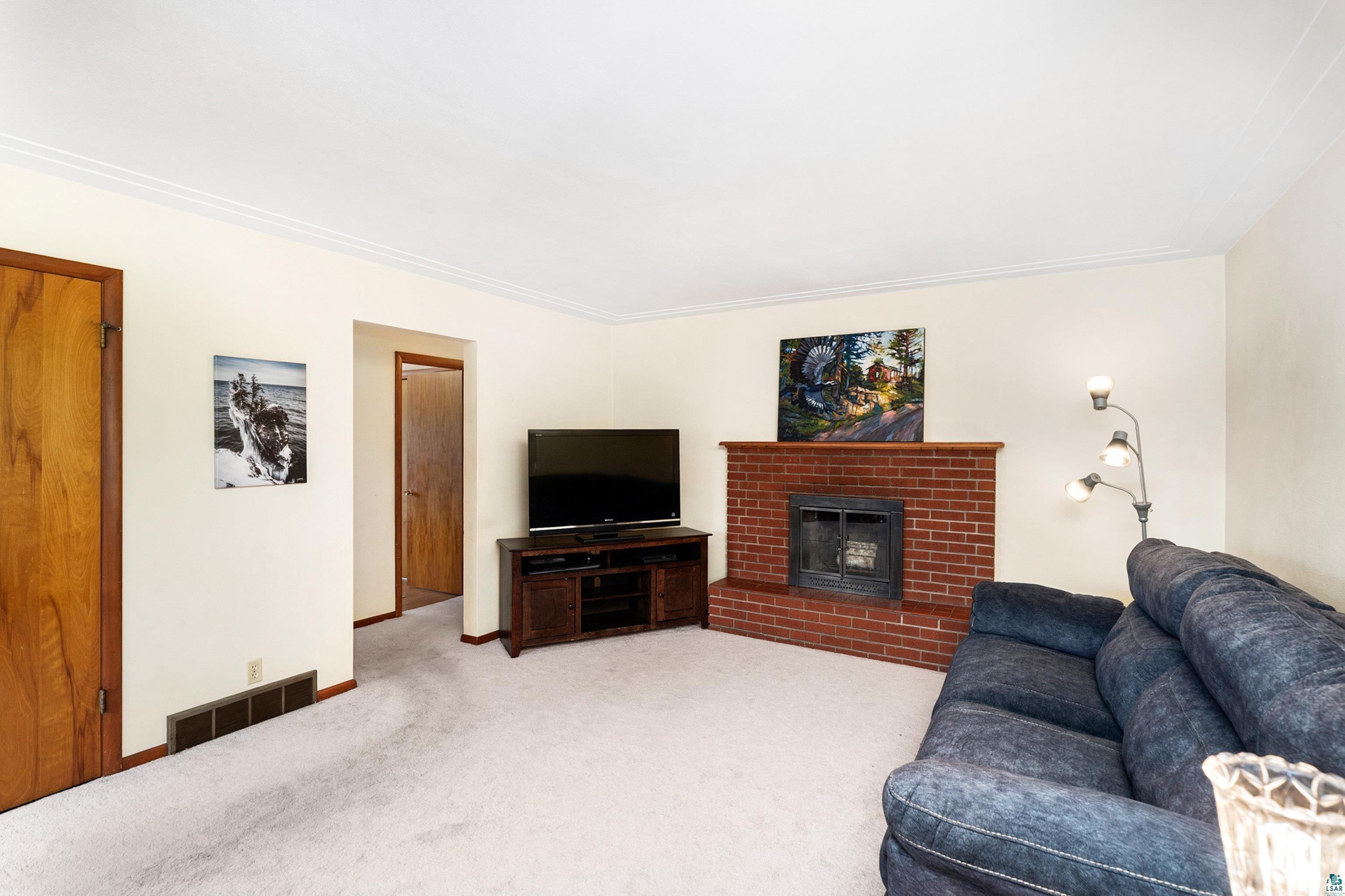4808 Midway Road Duluth, MN 55811 - Photo 19 of 57 Living area featuring a brick fireplace with a wood mantle, light-colored carpeting, and crown molding