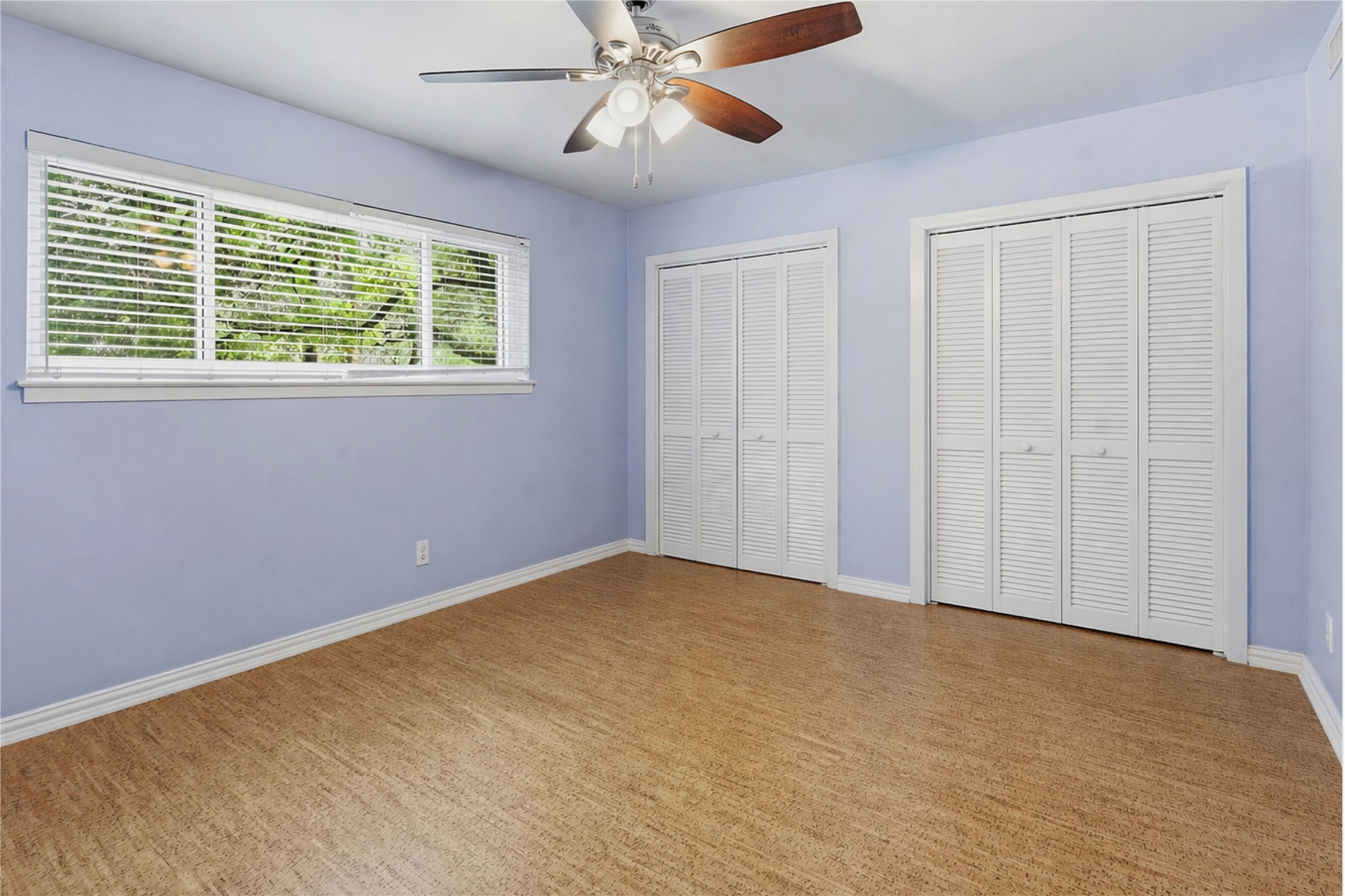 1210 Windsor Road, Unit 104 Austin, TX 78703 - Photo 20 of 27 Room featuring wood-finish flooring, a multi-pane window with horizontal blinds, two bi-fold louvered closets, and a ceiling fan with light fixture