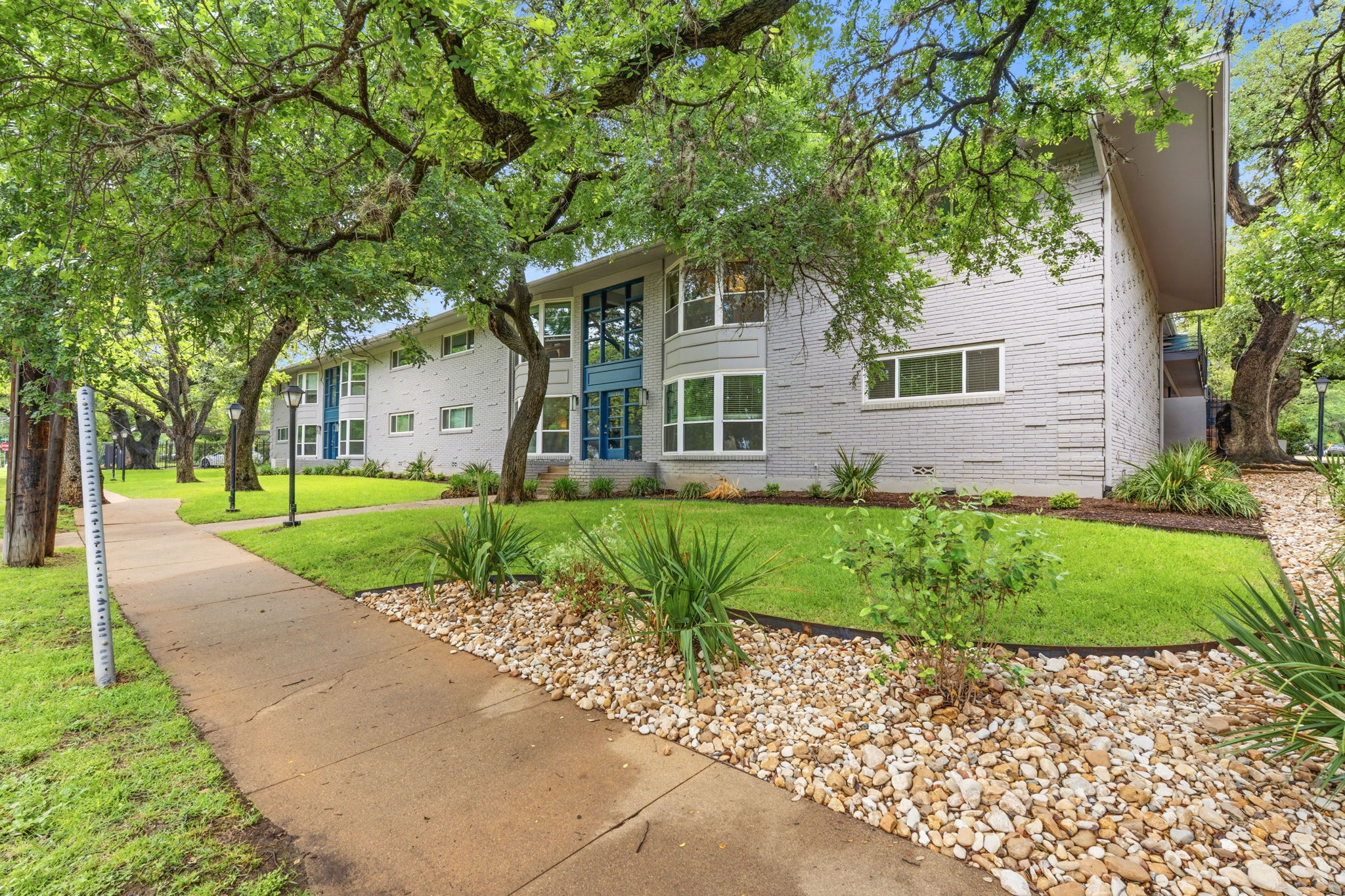 1210 Windsor Road, Unit 104 Austin, TX 78703 - Photo 27 of 27 Contemporary building exterior featuring light grey brick, expansive windows, and mature trees providing natural shade