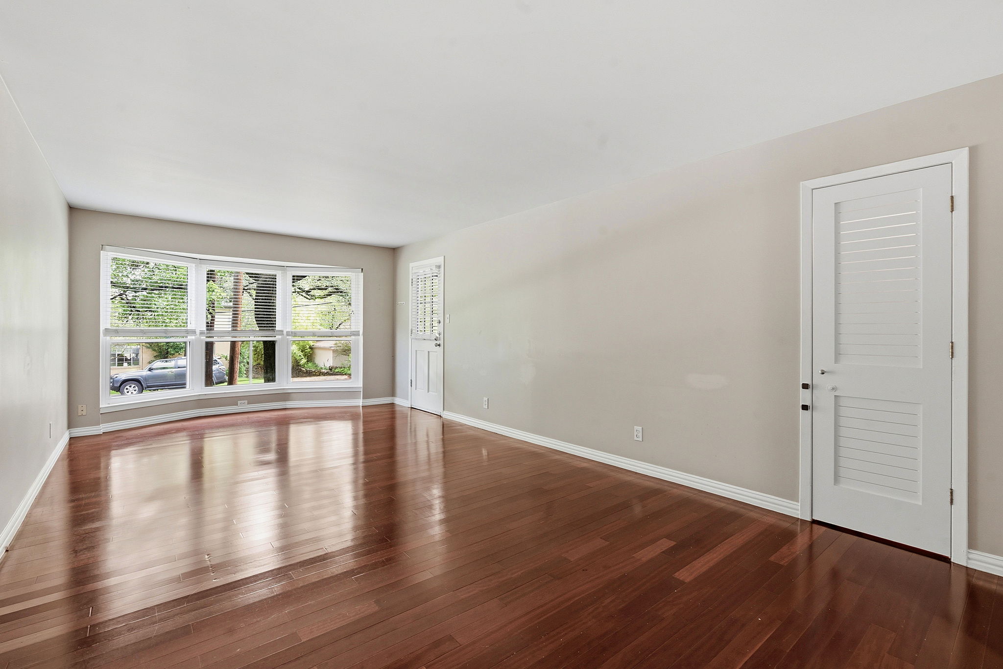 1210 Windsor Road, Unit 104 Austin, TX 78703 - Photo 5 of 27 Spacious room featuring wood-finish flooring, a curved bay window, white baseboards, and a white louvered door