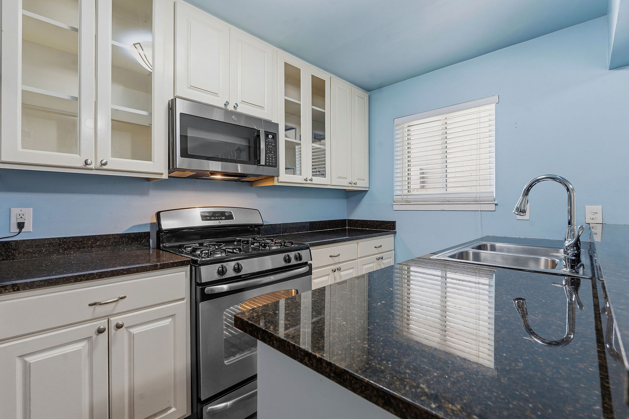 1210 Windsor Road, Unit 104 Austin, TX 78703 - Photo 10 of 27 Kitchen featuring dark countertops, stainless steel appliances, white cabinetry, and a double basin sink with a chrome faucet