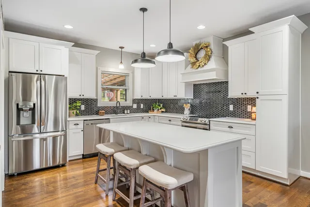 a kitchen with stainless steel appliances granite countertop a sink a stove a refrigerator and white cabinets with wooden floor