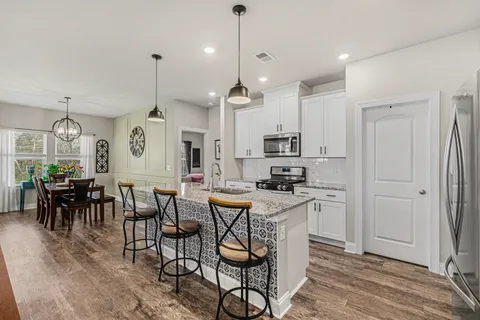 a kitchen with stainless steel appliances kitchen island granite countertop a dining table chairs stove and white cabinets