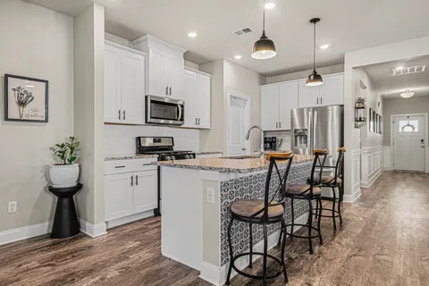 a kitchen with stainless steel appliances kitchen island granite countertop a refrigerator a stove a microwave oven a sink with island and chairs with wooden floor