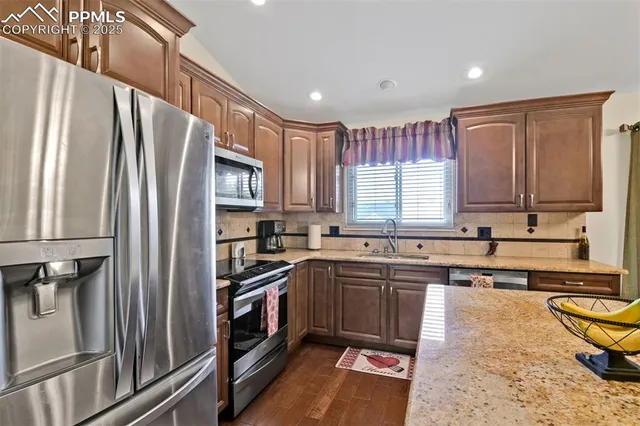 a kitchen with stainless steel appliances granite countertop a refrigerator a sink a stove a washer and wooden cabinets