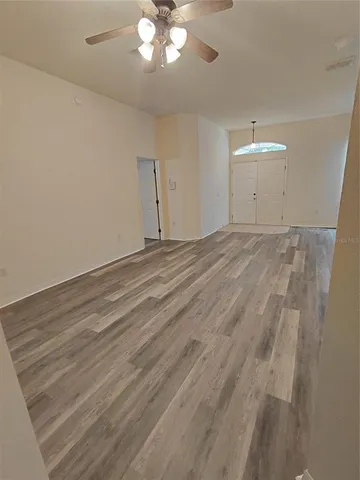 an empty room with a chandelier fan and wooden floor