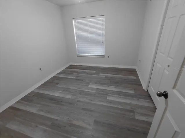 a view of an empty room with wooden floor and a fan
