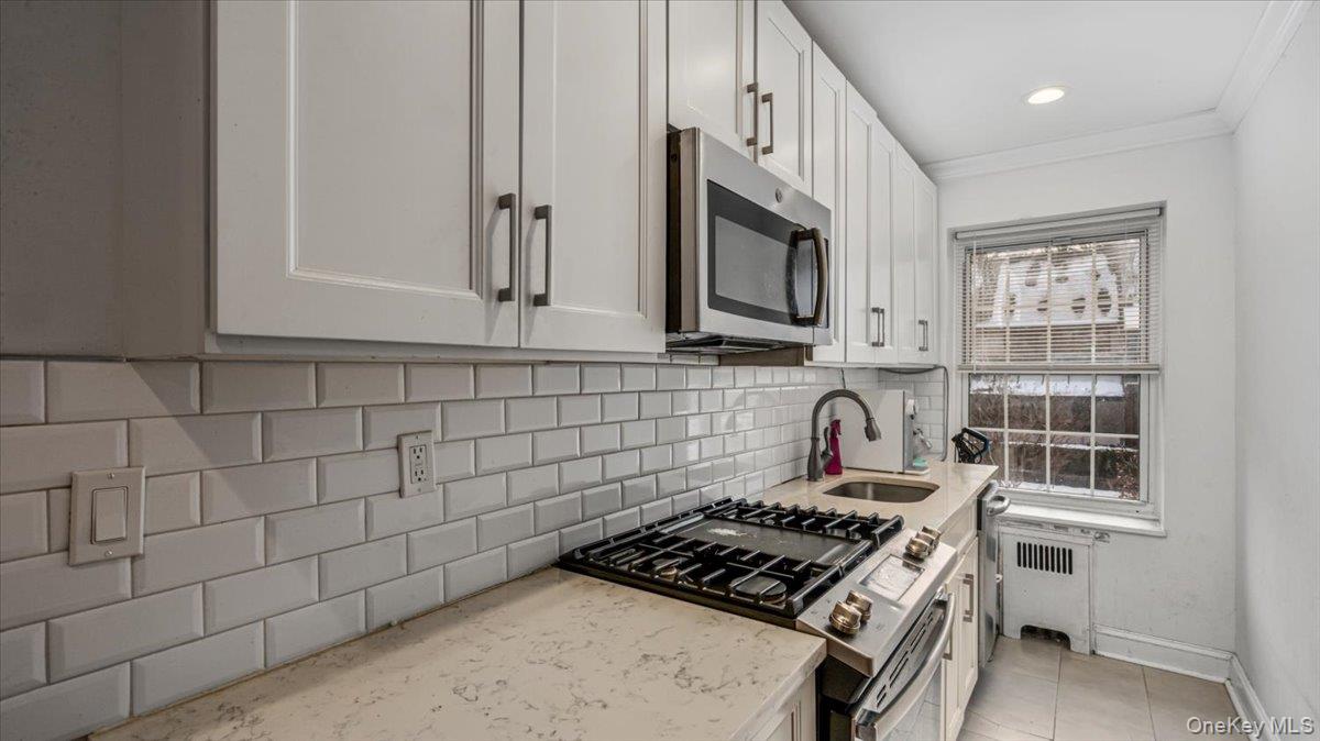 Kitchen with white cabinetry, appliances with stainless steel finishes, radiator, and sink