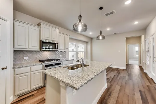 a kitchen with stainless steel appliances granite countertop a sink stove and white cabinets with wooden floor