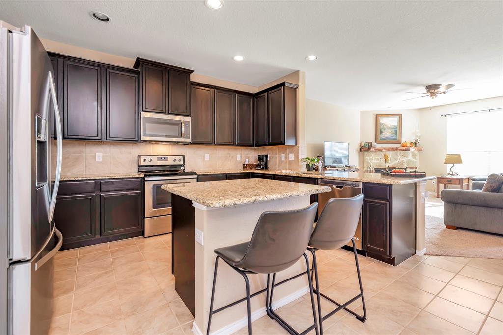 a kitchen with stainless steel appliances granite countertop a stove top oven a sink refrigerator and chairs