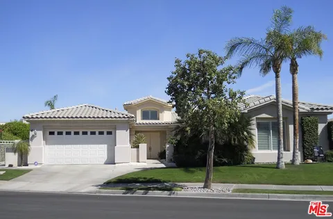 a front view of a house with a garden and palm trees