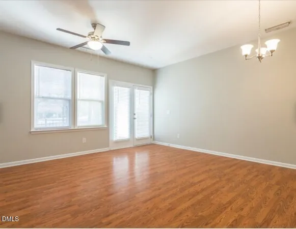 an empty room with wooden floor fan and windows