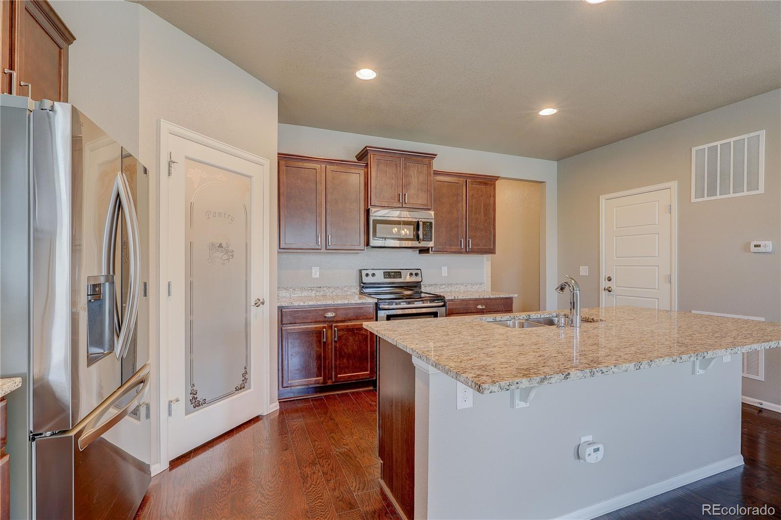 8891 Foxfire Street Firestone, CO 80504 - Photo 15 of 37 a kitchen with stainless steel appliances granite countertop a refrigerator a stove and a sink with wooden floor