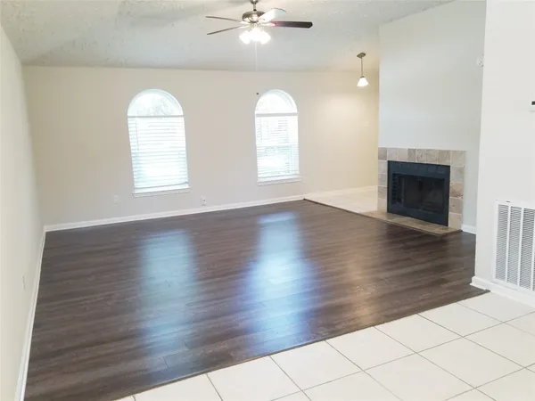 an empty room with wooden floor chandelier fan and windows