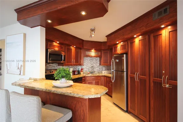 a kitchen with stainless steel appliances granite countertop a refrigerator a sink dishwasher a stove and a dining table with wooden cabinet
