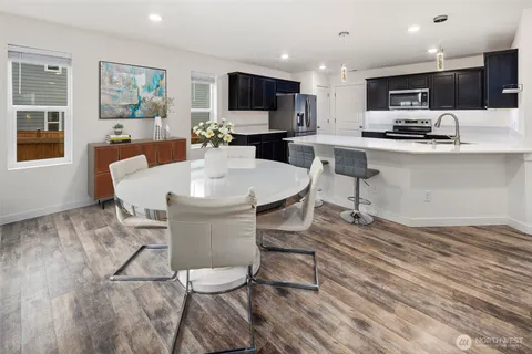 a kitchen with stainless steel appliances kitchen island granite countertop a stove a sink a microwave a refrigerator a dining table and chairs with wooden floor