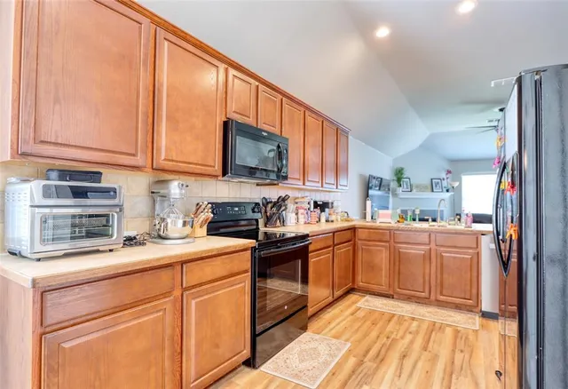 a kitchen with stainless steel appliances granite countertop a stove top oven a sink dishwasher and a refrigerator with wooden cabinets