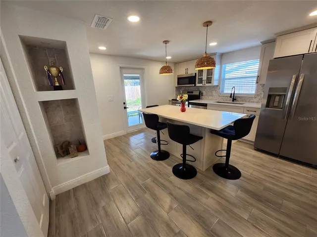 a kitchen with stainless steel appliances kitchen island granite countertop a sink dishwasher and a refrigerator with wooden floor