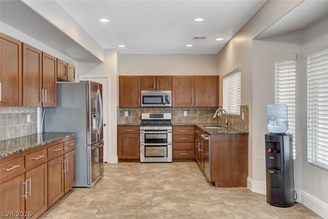 191 Verde Ridge Court Henderson, NV 89012 - Photo 12 of 36 Kitchen with appliances with stainless steel finishes, a sink, brown cabinetry, dark stone counters, and recessed lighting