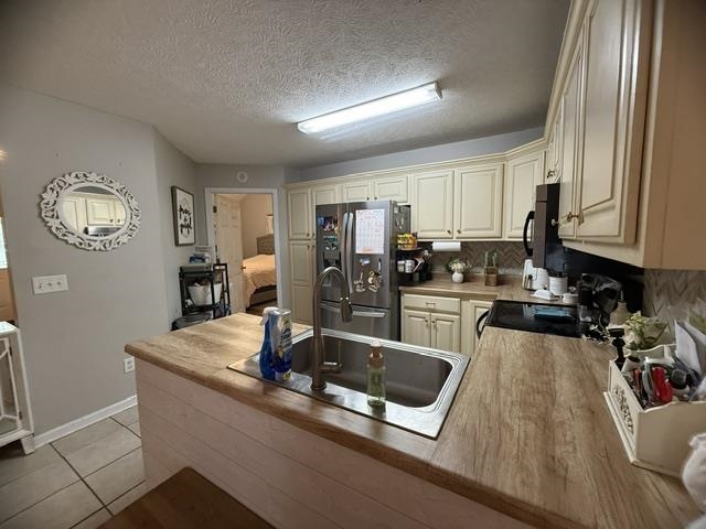 395 Austin Street Savannah, TN 38372 - Photo 6 of 32 Kitchen featuring wood-finish countertops, stainless steel sink with gooseneck faucet, light cabinetry with gold-tone hardware, and a herringbone-patterned backsplash
