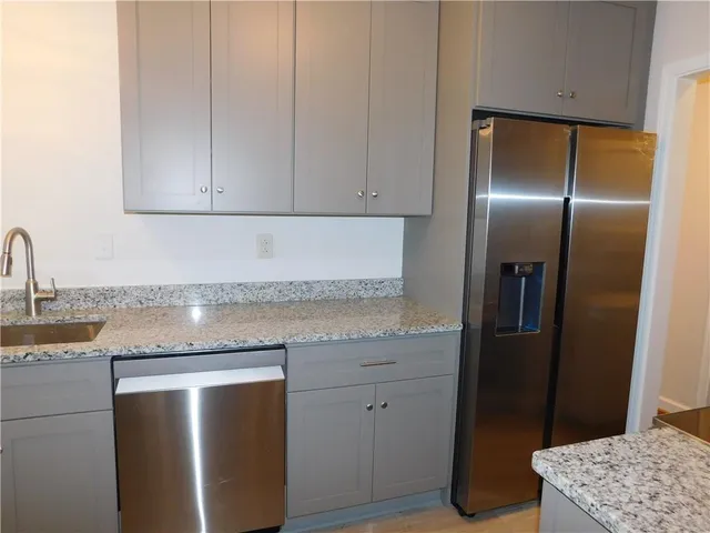 a kitchen with stainless steel appliances granite countertop a refrigerator a sink and white cabinets
