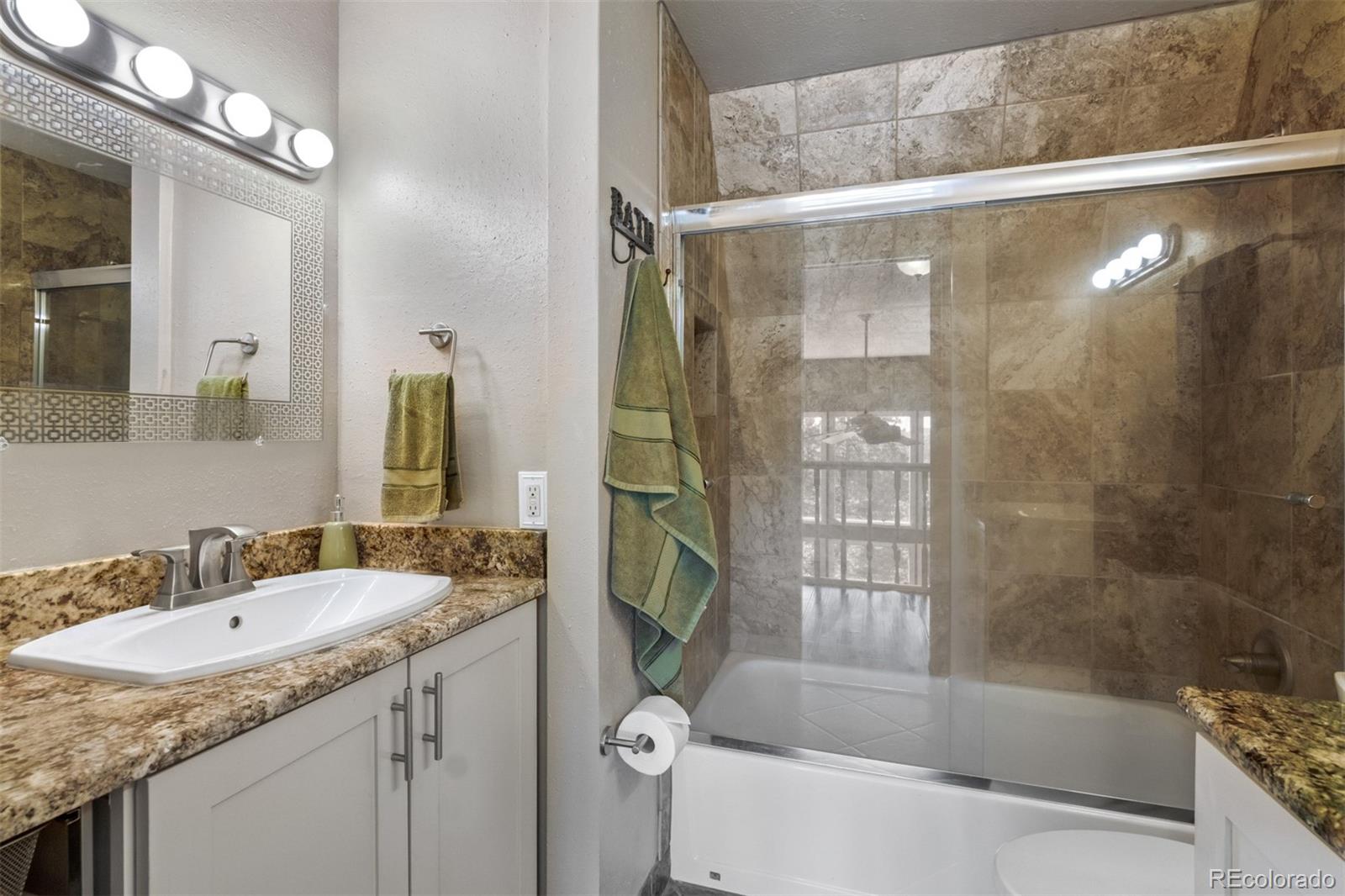 6637 High Drive Morrison, CO 80465 - Photo 16 of 28 a bathroom with a granite countertop sink a mirror a bathtub and shower